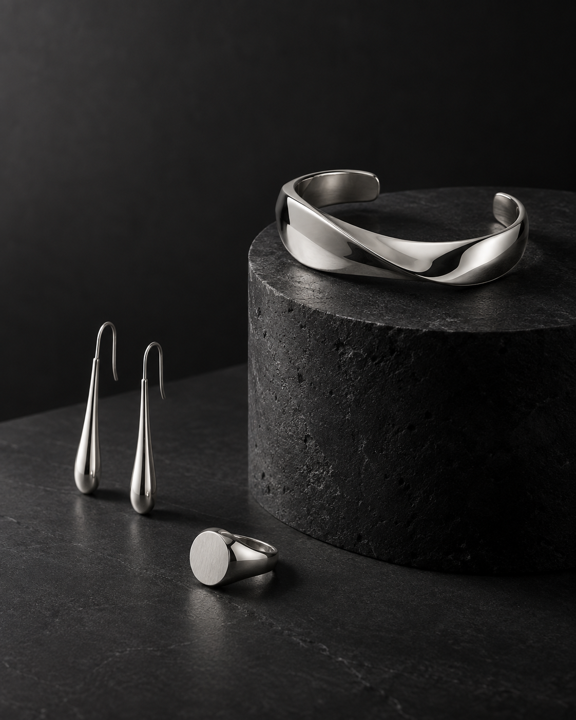 Silver cuff, drop earrings and signet ring on black stone