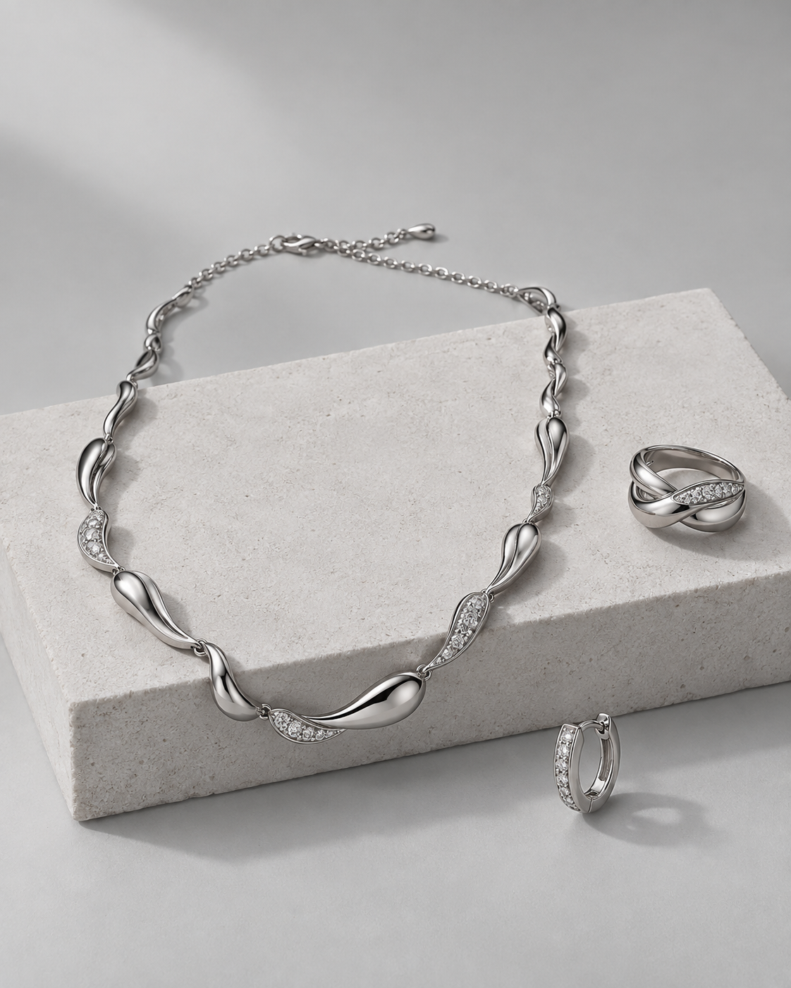 Silver necklace, ring and hoop earring on pale stone
